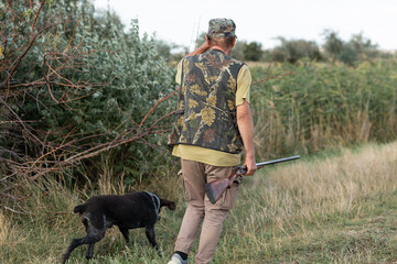 A hunter with his dogs, a spaniel and a german pointer, walk along the reeds in search of a...