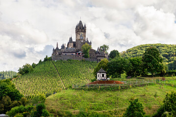 Cochem, Germany - September 9, 2025: The Reichsburg Cochem castle overlooks the steep, terraced vineyards and a small half-timbered house on the green hillside of the Moselle Valley, Germany