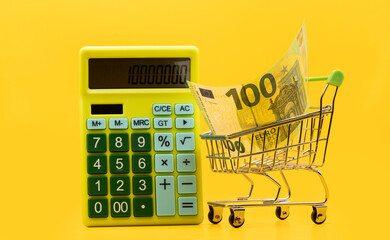 100 euro banknote in a shopping cart and calculator on a yellow background