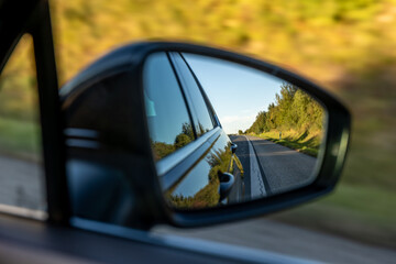 Car mirror view of country road. Travel with green landscapes.
