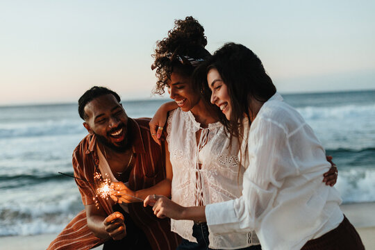 Friends sharing joyful moments holding sparklers by the beach at sunset - Powered by Adobe