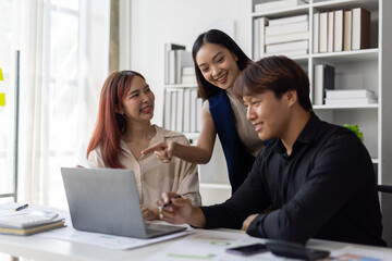 Asian business team analyzing data on laptop in office meeting.