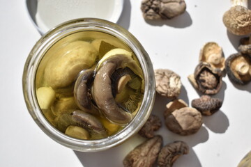 Open jar of pickled mushrooms among dried mushrooms, top view