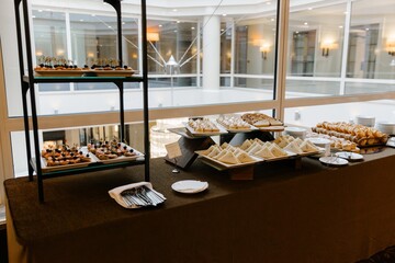 Elegant buffet table set up with a variety of appetizers, mini sandwiches, croissants, and desserts during a coffee break or corporate event in a sunlit modern interior
