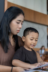 Obraz premium Close shot of a mother and toddler pointing at a menu together at a restaurant table, soft natural light and candid interaction.