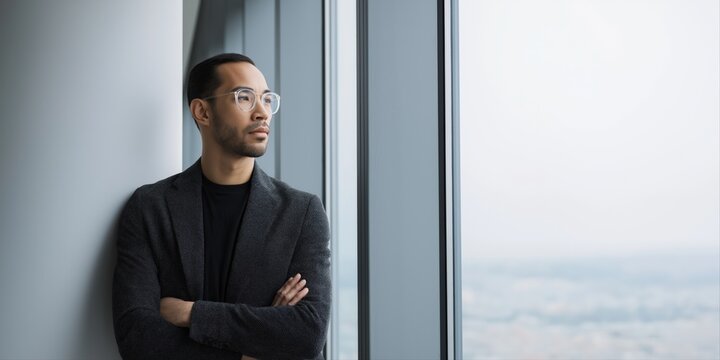 Contemplative asian male adult in office attire looking out window