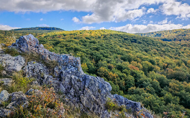Rocky limestone ridge above the colorful autumn forest near Odvas-kő, Bükk Mountains, Hungary. Bright light and rolling hills under a vivid blue sky.