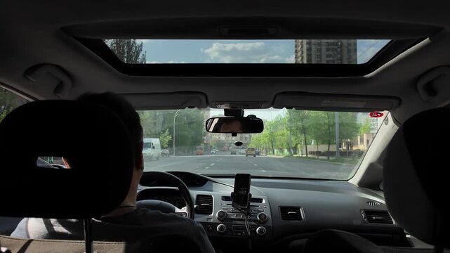 Inside a car a man is driving on a city road on a sunny day