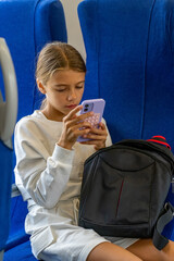 Focused young girl with blonde hair sitting in blue-seated vehicle, engrossed in her purple...