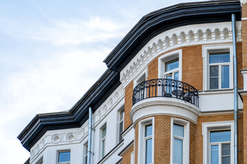 Elegant historical architecture of urban building, showcasing intricate white moldings, warm brickwork, curved balcony with iron railing, and dark roofline against serene sky. © sommersby