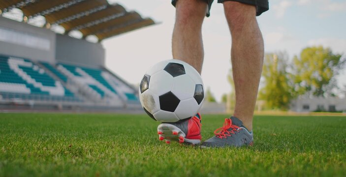 Soccer player balancing football on foot on green grass field in modern stadium, symbol of training, control, and athletic performance