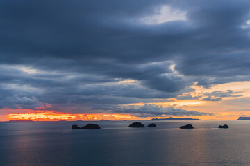 Calm Sea with Cluster of Small Islands beneath Dramatic Cloud Layers and Glowing Orange Horizon Light, Peaceful Tropical Concept