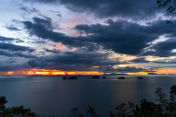 Fiery Orange Sunset over Ocean with Dark Dramatic Clouds and Islands Silhouetted on Horizon, Tranquil Seascape and Beauty Concept