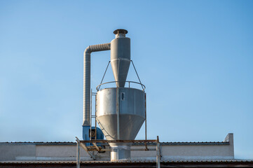 Industrial metal chimney and ventilation system on factory rooftop under clear blue sky.