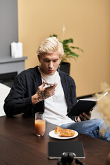 Young man enjoying breakfast in a stylish apartment while reading quietly