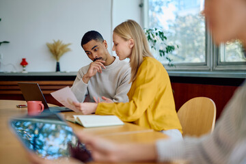 Multi-ethnic colleagues analyzing documents and discussing strategy around a table in a modern office environment