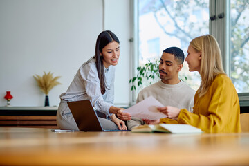 Diverse business professionals reviewing documents and using a laptop during an informal work meeting in a modern office space