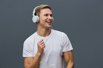 Smiling man wearing white t-shirt and wireless headphones, joyful expression, hands clenched in...