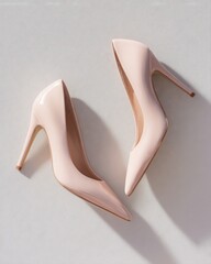 Two pale pink patent leather stiletto pumps rest on a light textured surface casting dramatic shadows.