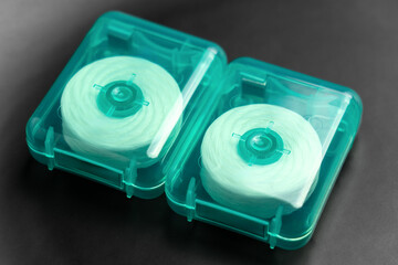 Two rolls of dental floss in green plastic cases on black close up