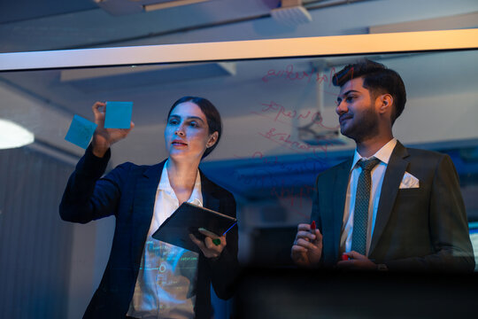 Businessman and businesswoman corporate professional brainstorming , discussing ideas, innovation technology, and writing on glass board in modern office