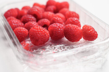 Fresh raspberries in plastic transparent supermarket packaging on a white table surface