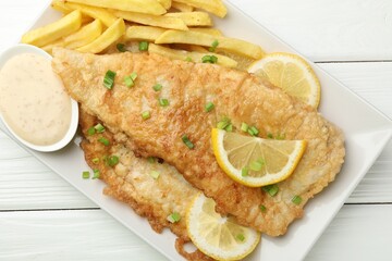 British Traditional Fish and chips with sauce, lemon and green onion on white wooden table, top view