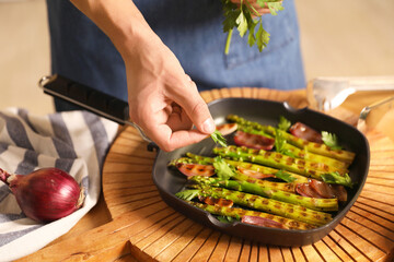 Man adding parsley into pan with grilled vegetables at table indoors, closeup