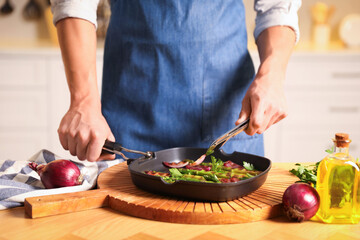 Man adding onion into pan with grilled vegetables at table indoors, closeup