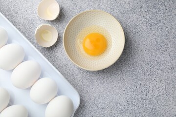 Many whole raw chicken eggs and broken one in bowl on grey table, flat lay