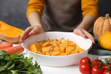 Woman with pieces of fresh pumpkin and ingredients at white wooden table, closeup