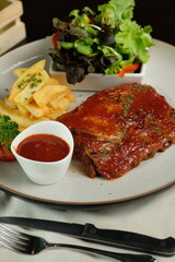 Delicious grilled ribs, french fries, salad, and a sauce, all served on a plate ready to enjoy. A culinary creation, perfect for food enthusiasts.