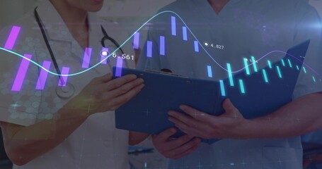 Two doctors in scrubs analyzing digital graphs in clinic hallway, with stethoscope and blue folder