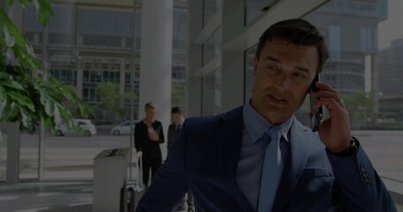 Talking Asian businessman wearing navy suit using smartphone in lobby with glass wall, copy space