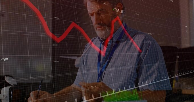 Writing senior male analyst taking notes in notebook at office desk, with financial data overlay