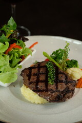 A culinary masterpiece: a grilled steak with accompanying fresh vegetables. The steak sits atop a bed of creamy mashed potatoes, with a side of mixed greens.