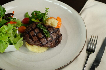A delicious steak dish with vegetables, finely plated with a fork and knife. The meal includes a juicy grilled steak and a fresh salad