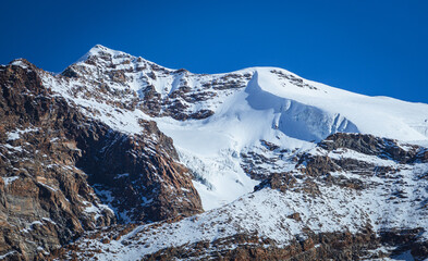 Stunning autumn landscape in Alta Val d'Ayas, Aosta Valley. Scenic view of Monte Rosa glaciers and a rushing mountain stream flowing through golden larch forests under a sunny blue sky in the Alps.
