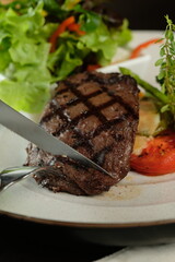 A close-up view of a grilled steak, expertly cut with a knife, accompanied by fresh salad and vegetables on a plate