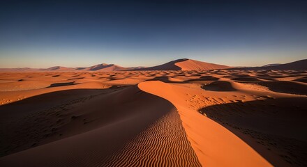 Vast orange sand dunes under a clear blue sky in a remote desert landscape at sunrise or sunset