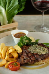 A close-up shot of a gourmet steak, served with fries, sauce, and a glass of wine