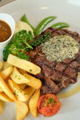A mouthwatering grilled steak, garnished with herb butter and served with golden fries, vegetables, and gravy. The dish looks delicious and ready to be enjoyed