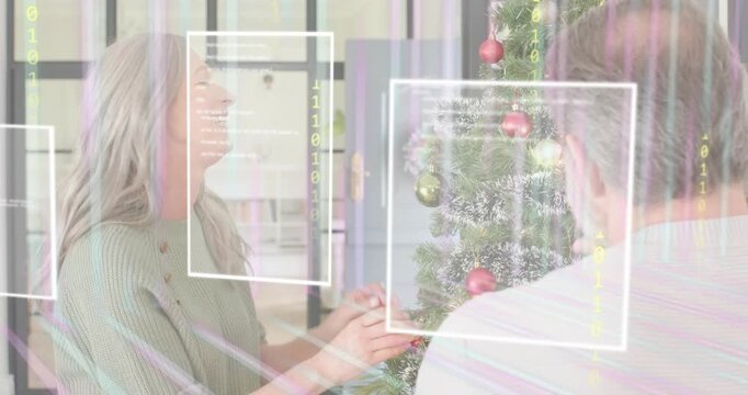Senior woman selecting bauble triggers AR frames and binary streams while couple decorating tree