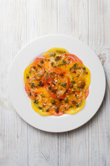 Tomato carpaccio with sun-dried tomatoes, capers and green sauce on a white plate on the table. Fresh salad. Healthy eating concept. Modern dish. Vertical orientation. Top view