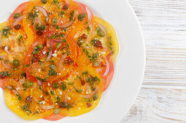Tomato carpaccio with sun-dried tomatoes, capers and green sauce on a white plate on the table. Fresh salad. Healthy eating concept. Modern dish. Horizontal orientation. Top view. Copy space