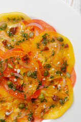 Tomato carpaccio with sun-dried tomatoes, capers and green sauce on a white plate on the table. Fresh salad. Healthy eating concept. Modern dish. Vertical orientation. Top view. Close up