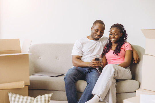 African couple relaxing on couch with phone during moving day