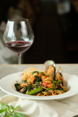 Delicious pasta with mussels and a glass of red wine, culinary delights. The dish looks appetizing on a white plate with fresh basil leaves next to a glass of red wine