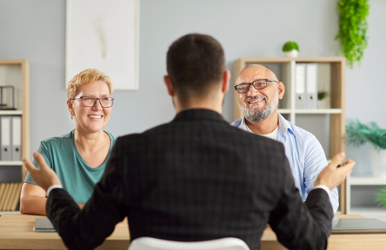 Fototapeta Smiling senior couple consults a financial advisor in office, reviewing paperwork and signing documents during a meeting. Male agent consulting elderly clients about investments and insurance. 