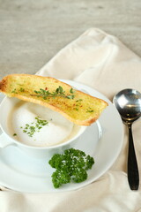 A delicious cream soup with a slice of garlic bread and a spoon, ready to be enjoyed. The soup and bread arranged on a white plate with parsley